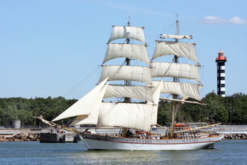 Fototapeta na wymiar A large sailboat with sails leaves the port area