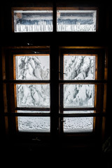 A view of the mountains through a wooden window in a mountain cottage.
