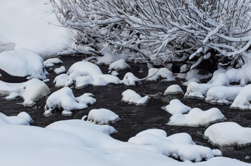 Winter river with icy stones and banks covered with white snow on a cloudy day