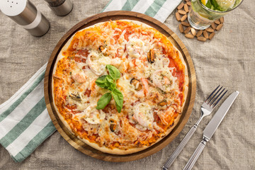 Pizza with seafood, mozzarella, mussels, octopus, squid, salmon, shrimp serves on the table