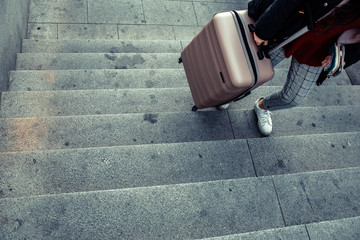 Woman dragging a trolley suitcase to climb the stairs of a subway.