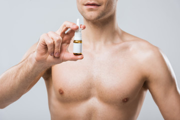 cropped view of shirtless man holding nose spray, isolated on grey