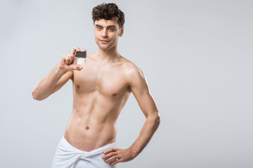 Fototapeta na wymiar shirtless man holding bottle of perfumes, isolated on grey
