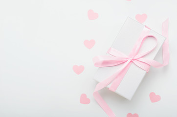 White gift box with pink ribbon and hearts on a white background. Valentine's day gift, women's day. Copy space, top view, flat lay.