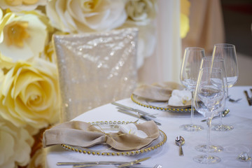 Fototapeta na wymiar Sitting arrangement at a formal event or fine dining restaurant featuring transparent plates with golden details, glassware and silverware in the order of use set against a paper flowers wall