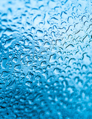 Natural water raindrops on glass window after rain over the blue background. Abstract texture with water drops on window