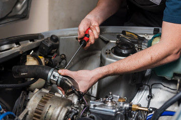 Man's hands with a screwdriver repairing the old car inside of the garage.