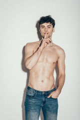 Fototapeta premium sexy shirtless man in jeans showing silence symbol while posing on grey