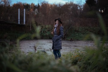 Fototapeta premium A girl stands on the bank of the river at the bridge on a cloudy evening.