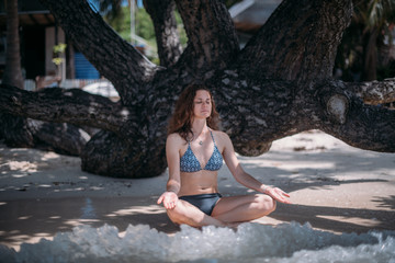 Young slim girl sitting in the shade of a tree in the sea waves on the coast of a tropical island