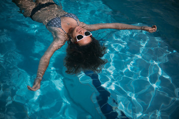 A young girl in sunglasses swims in the pool. Beautiful woman resting in the water in the outdoor pool
