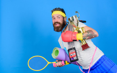 Choose sport you like. Man bearded athlete hold sport equipment jump rope fitness mat boxing glove expander racket and golden goblet. Sport shop assortment. Sport concept. Get body ready for summer