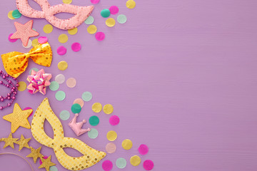 carnival party celebration concept with mask and colorful party accessories over purple wooden background. Top view. Flat lay.