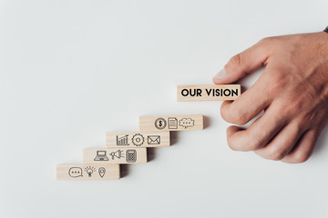 cropped view of man holding wooden block with words 'our vision' on top of wooden bricks with icons isolated on white