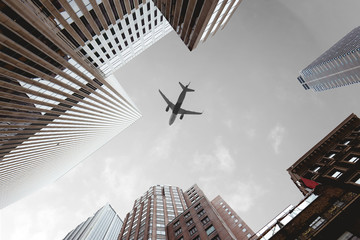 Fototapeta na wymiar bottom view of skyscrapers and airplane in cloudy sky in new york city, usa