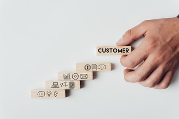 cropped view of man holding wooden block with word 'customer' on top of wooden bricks with icons isolated on white