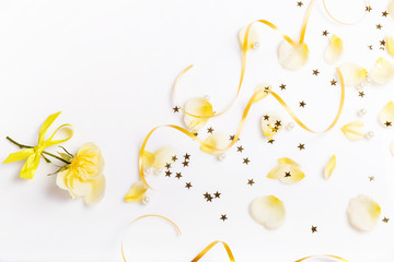 Beautiful bright yellow petals are flying on white background and a rose with ribbon, creative floral layout, horizontal. Overhead top view, flat lay.