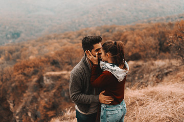 Cute couple in love standing at viewpoint at autumn and kissing. In background forest and mountains.