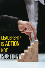 cropped view of woman climbing with fingers wooden career ladder, 'leadership is action not position' lettering on foreground