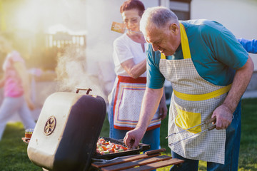 Older cheerful couple making barbeque in backyard. Spending some time with their family.
