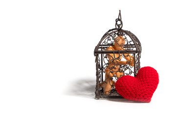 Action figure sitting in cage and there is a red heart on the outside on white background. Concept of Love, imprisonment and deprivation