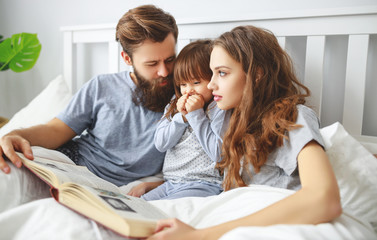 happy family mother, father and child read a book, a fairy tale  in bed