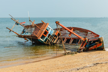 a broken fishing ship lies on its side near the shore, shipwrecked