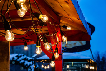 Decor of a garland of incandescent lamps on the roof of a street shop