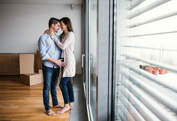 Young couple with cardboard boxes moving in a new home, hugging. Copy space.