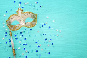 carnival party celebration concept with elegant gold mask on stick over mint wooden background and stars. Top view.