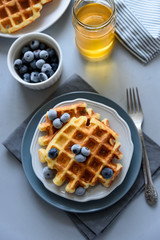 Belgian waffles with blueberries and honey on gray wooden background. Homemade healthy breakfast. Selective focus