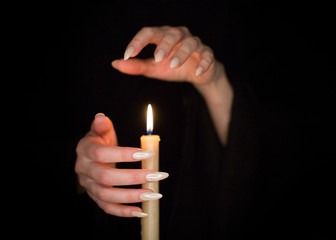Candle and female witch hands with sharp pearl nails. Divination and witchcraft, low key.