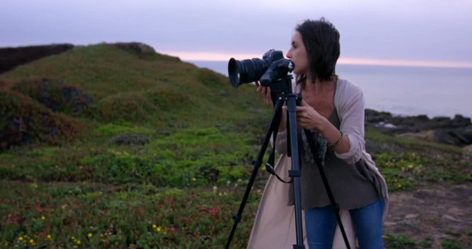 Young female Photographer sets up camera tripod in front of beautiful ocean landscape