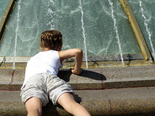 Little girl playing with water in the fountain. Child enjoying the summer, hot weather, happy childhood