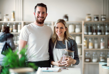 A portrait of two shop assistants standing in zero waste shop, looking at camera.