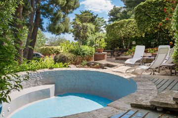 Sunbathing beds next to small pool full with clear blue water in the backyard of beautiful villa close to the sea. Concept of summer party, relaxation and luxury lifestyle.  