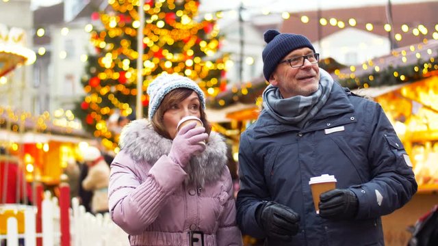 winter holidays and people concept - senior couple with takeaway hot drinks at christmas market on town hall square in tallinn, estonia