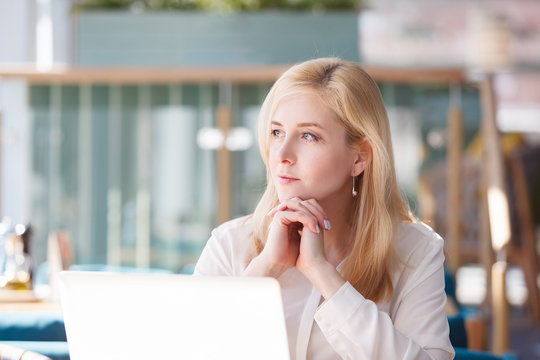 Portrait of thoughtful young blonde woman thinking about life about family and work and looking somewhere in the distance while sitting at the laptop during the working day