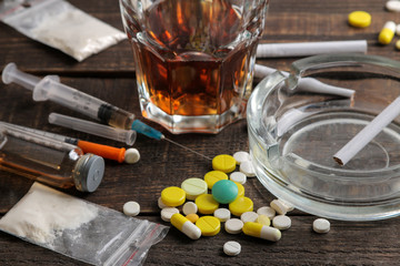 Various addictive drugs including alcohol, cigarettes, and drugs on a brown wooden table. Drug...