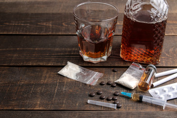 Various addictive drugs including alcohol, cigarettes, and drugs on a brown wooden table. Drug...
