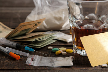 Various addictive drugs including alcohol, cigarettes, and drugs on a brown wooden table. Drug addiction concept