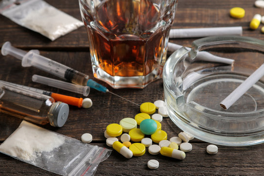 Various addictive drugs including alcohol, cigarettes, and drugs on a brown wooden table. Drug addiction concept