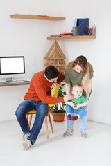 Concept of care. Young positive parents play with their happy little son at home near computer with a white screen. Place for text