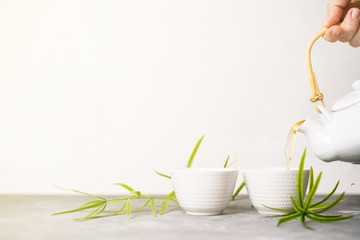 Female hand pouring green tea from a teapot into cups on white background with copy space. Asian tea set.