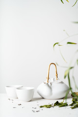 Asian tea concept, two white cups of tea and teapot surrounded with green tea dry leaves , space...