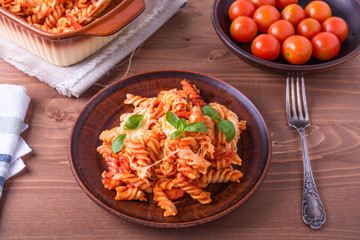 Portion of baked fusilli pasta with mozzarella cheese and tomato on a plate, top view, rustic style