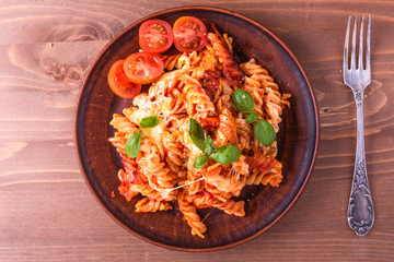 Portion of baked fusilli pasta with mozzarella cheese and tomato on a plate, top view, rustic style
