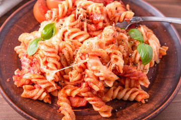 Portion of baked fusilli pasta with mozzarella cheese and tomato on a plate close-up, top view, rustic style
