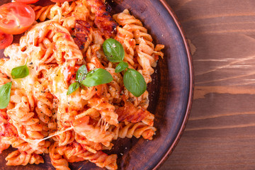 Portion of baked fusilli pasta with mozzarella cheese and tomato on a plate close-up, top view, rustic style, copy space for recipe