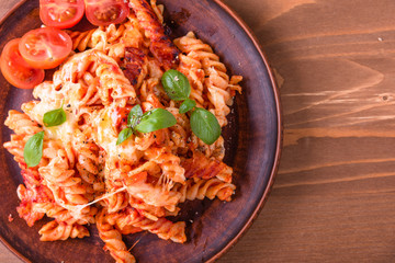 Portion of baked fusilli pasta with mozzarella cheese and tomato on a plate close-up, top view, rustic style, copy space for recipe